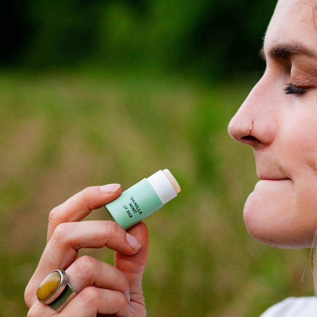 Good Flower Farm Lip Balm In Vanilla Mint With 100% Biodegradable Cardboard Tube, Being Applied By Woman With  Closed Eyes.