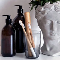 Truthbrush Soft Bamboo Toothbrushes in Cloud White, Shown in Small Glass on Countertop with Bottles and Planter.