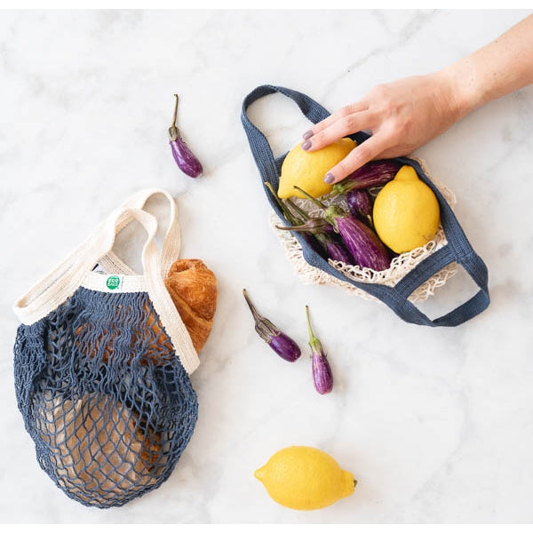 EcoBags Mini String Bag In Storm Blue, Shown With Woman Reaching For Lemon In Bag.