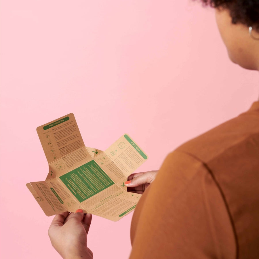 Woman Reading OganiCup Menstrual Cup Information Inside Kraft Cardboard Box Packaging.