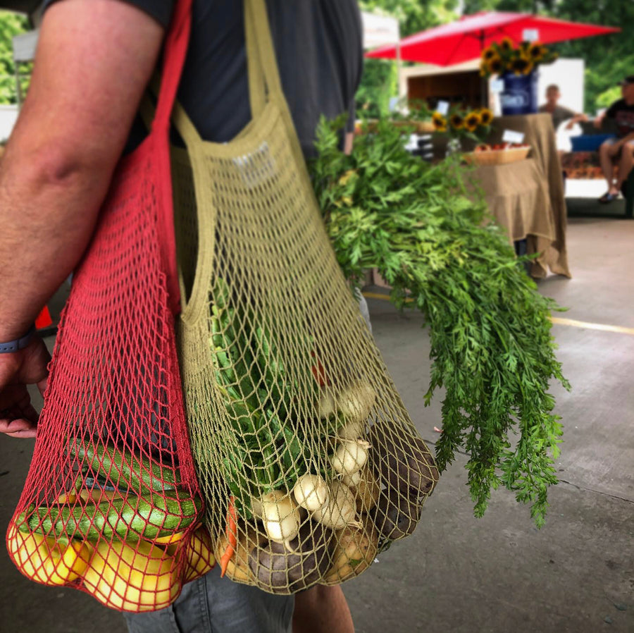EcoBags String Shopping Bags, Filled With Fresh Produce And Hanging From Man's Shoulder At Farmer's Market.